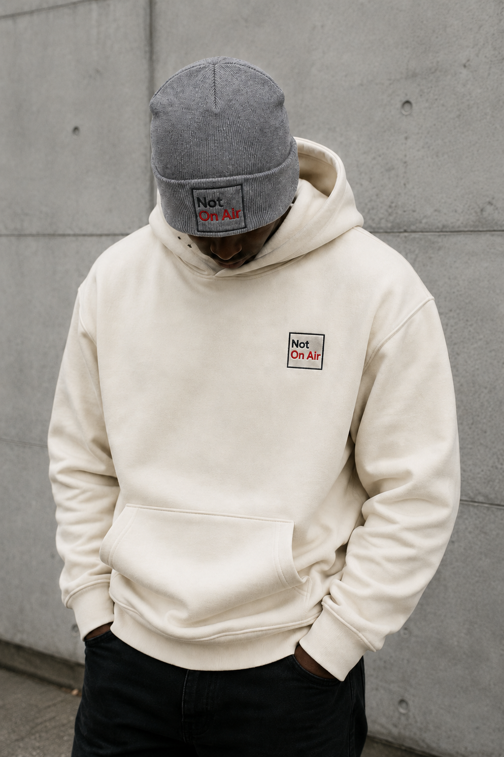 Faceless model wearing a gray embroidered Not On Air beanie and washed natural embroidered hoodie.