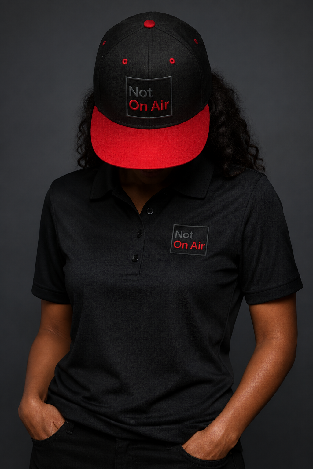 Faceless model wearing a black and red Not On Air embroidered snapback and black performance polo.